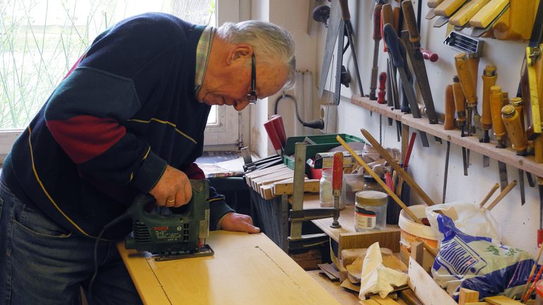 Ein Bewohner sägt in der Werkstatt mit einer Stichsäge etwas aus Holz