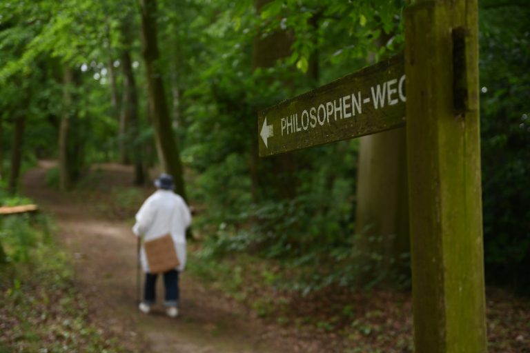 Bewohnerin spaziert durch den Wald, im Vordergrund steht ein Wegweiser