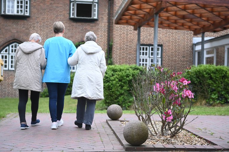 Bewohnerinnen laufen mit Pflegerin über das Gelände